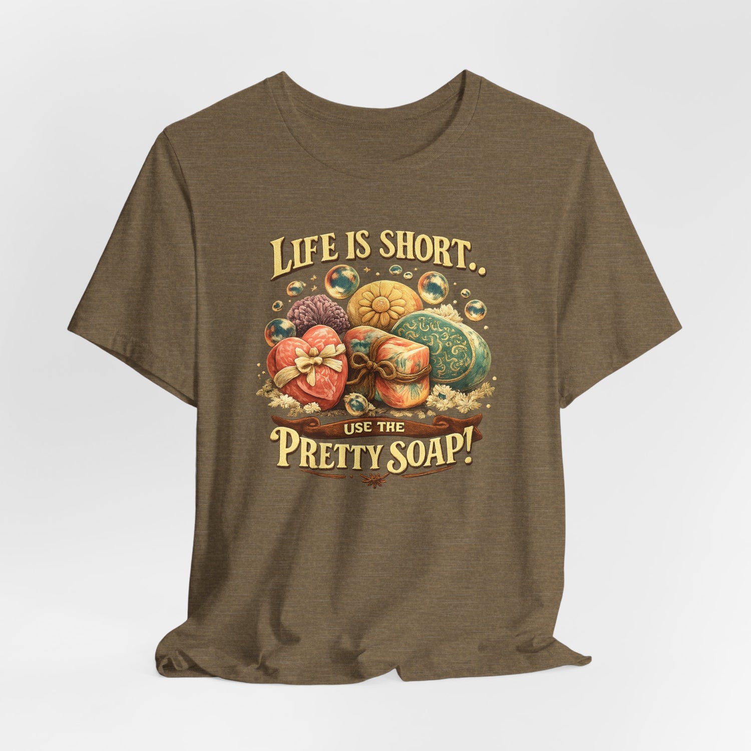 A brown t-shirt displays a graphic design that says, "Life is short, use the pretty soap!" with illustrations of colorful, decorative soaps.
