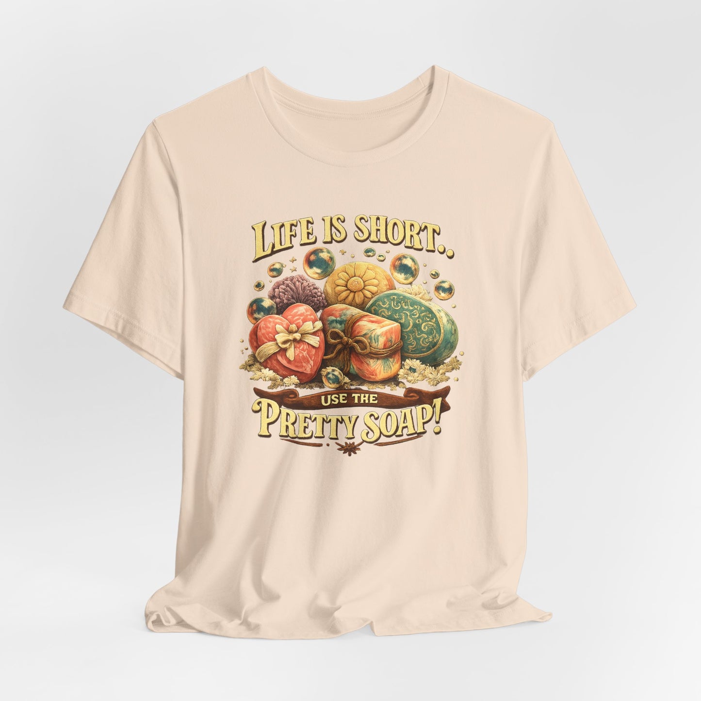 The t-shirt displays a vintage design with the text "Life is short, use the pretty soap!" surrounded by decorative artisan soap bars and bubbles.
