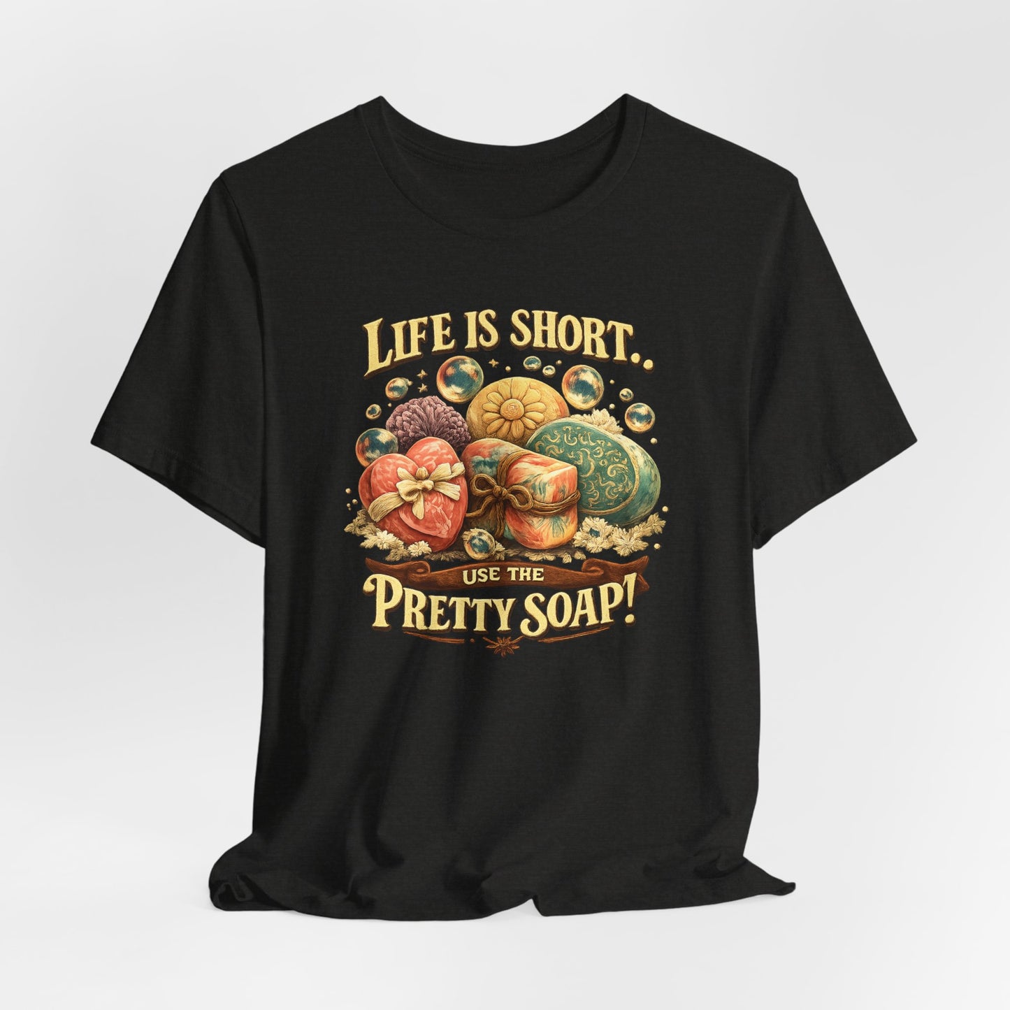 Showcase a black t-shirt featuring a design that says "Life is short, use the pretty soap!" with colorful, decorative soaps.
