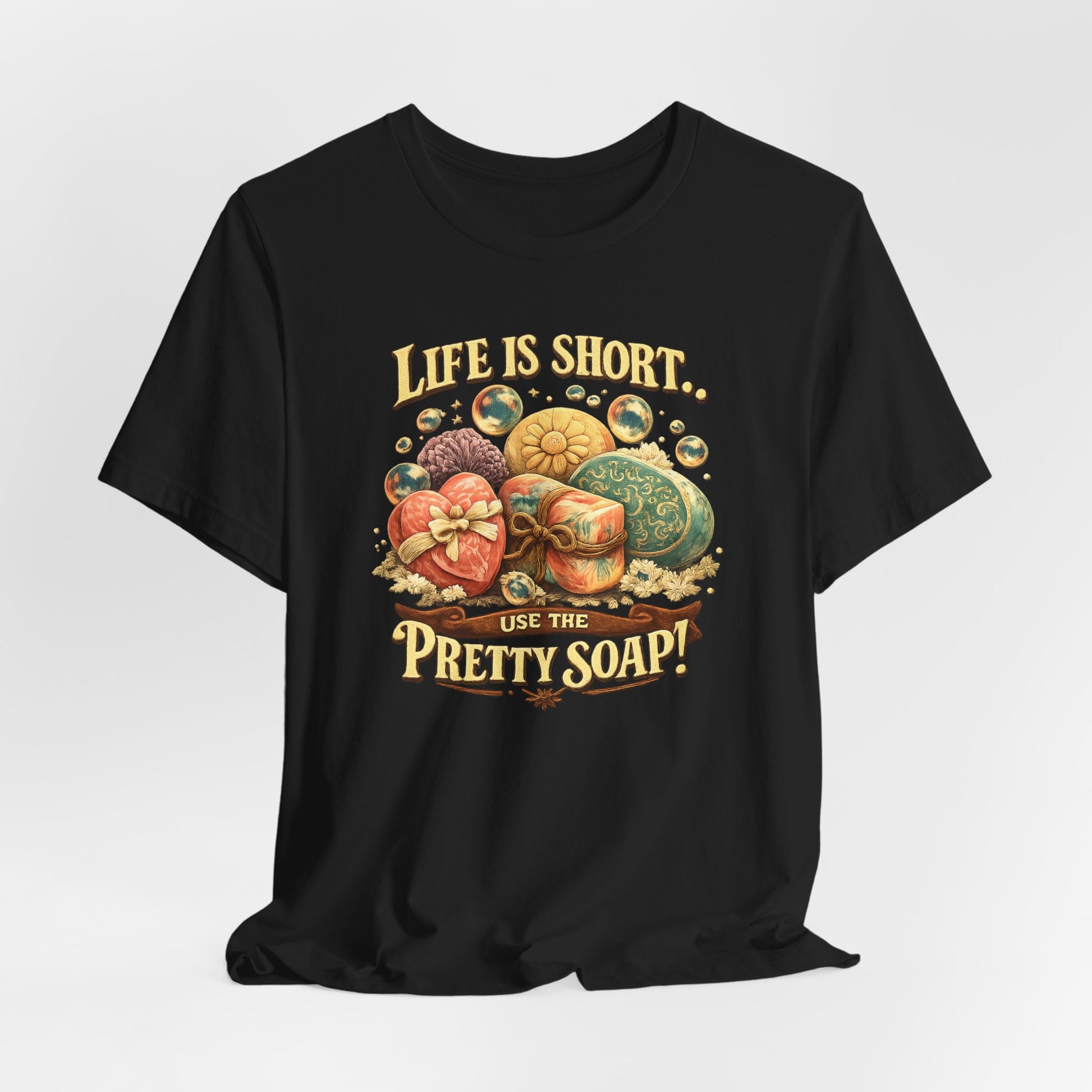 Black t-shirt displays an artistic design encouraging self-care with "Life is Short, Use the Pretty Soap!" above assorted decorative soaps.
