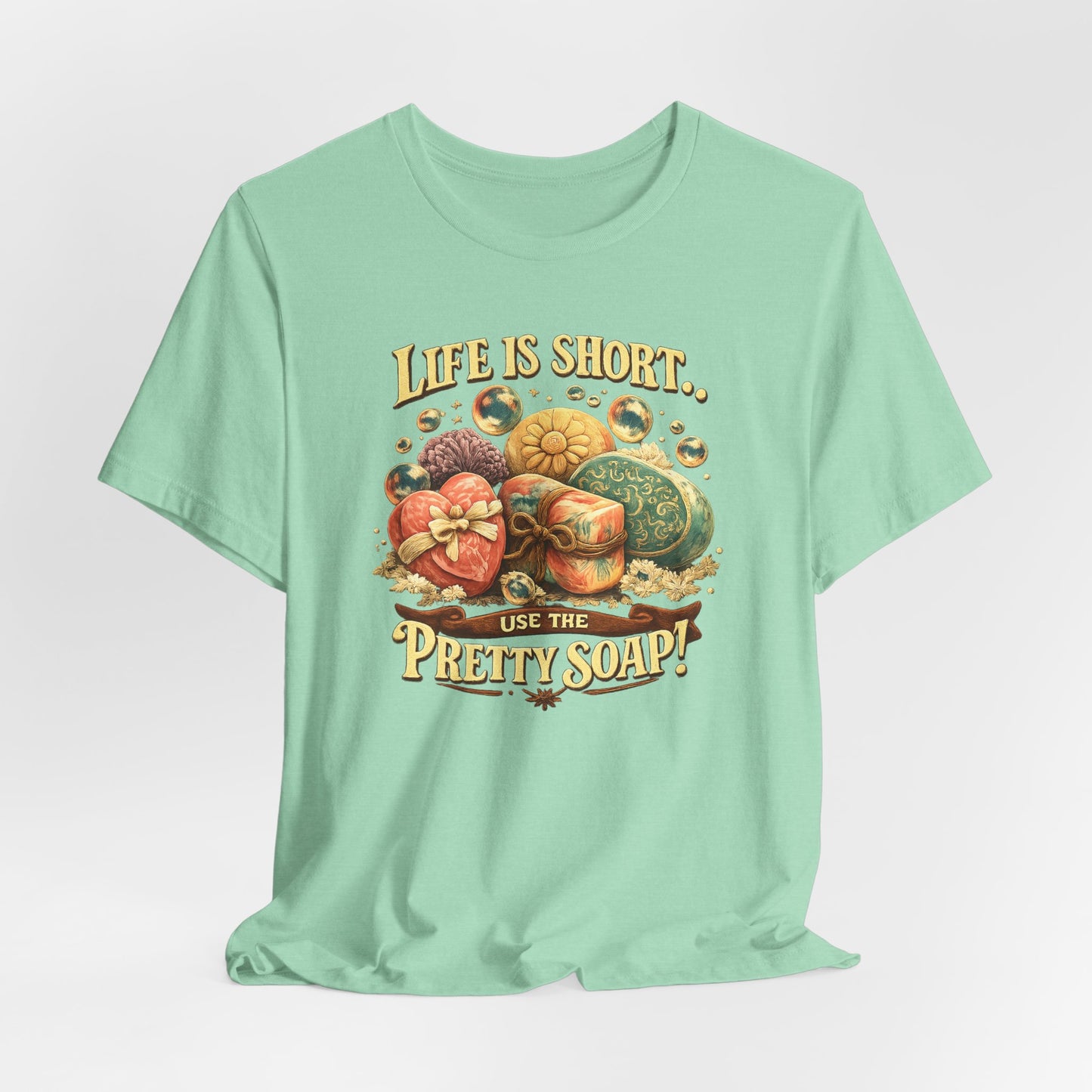 A mint green t-shirt displays a vintage-style graphic of assorted decorative soaps and the text "Life is short, use the pretty soap!".
