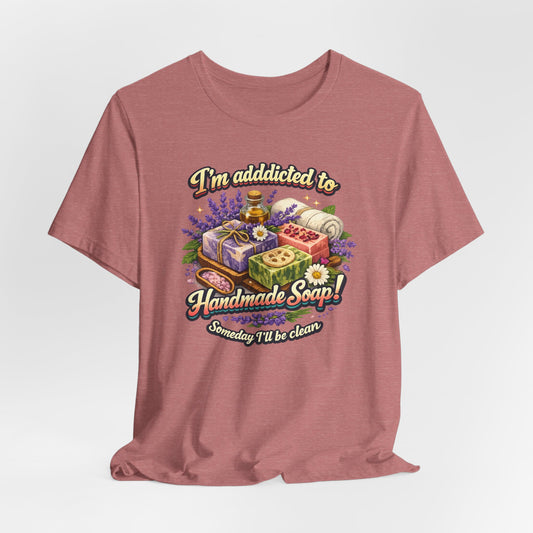 A dusty rose t-shirt displays a colorful graphic declaring "I'm addicted to Handmade Soap!" with an illustration of various soaps, flowers and bath salts.
