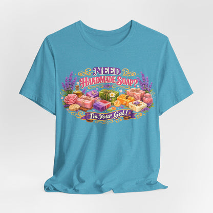Teal T-shirt displays "Need Handmade Soap? I'm Your Gal!" design with colorful artisanal soaps and botanicals.
