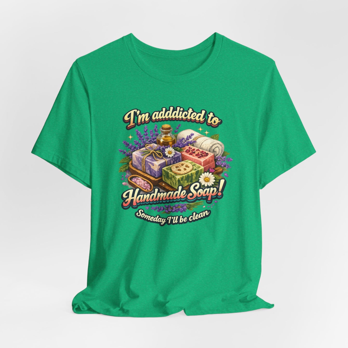 Green t-shirt features a graphic declaring addiction to handmade soap, alongside an illustration of artisanal soaps, essential oil, and lavender.
