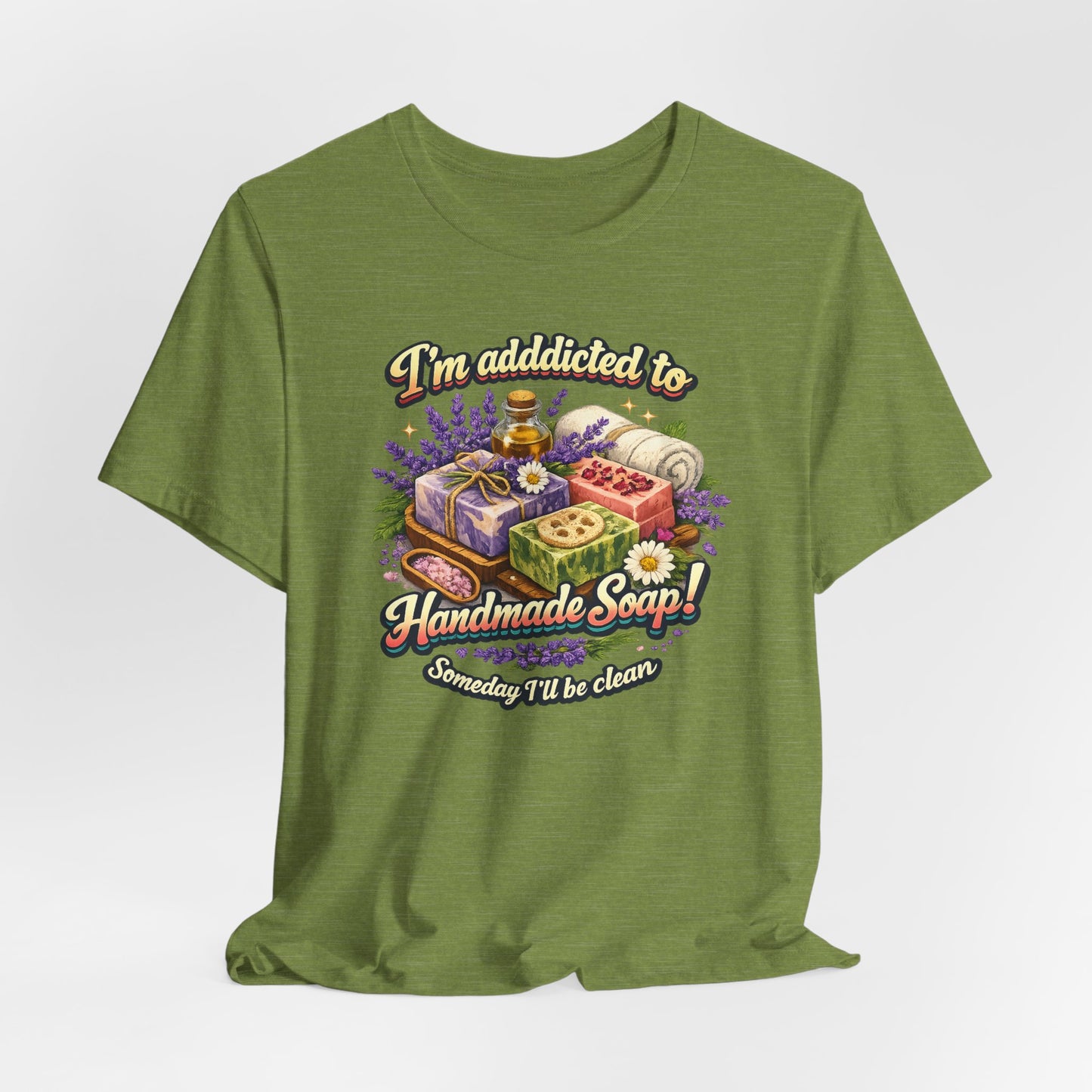 Olive green t-shirt displays an illustration with the phrase "I'm addicted to Handmade Soap! Someday I'll be clean", featuring handmade soaps, lavender, and bath salts.
