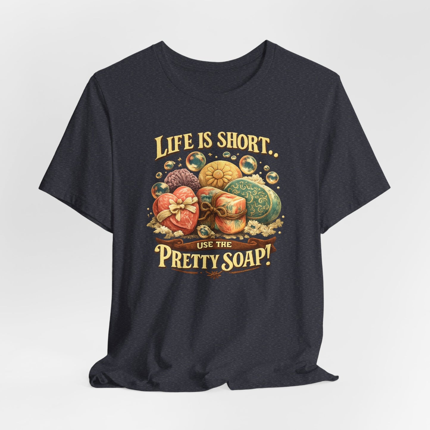 Displays a dark blue t-shirt featuring an illustration promoting handcrafted soaps with the phrase "Life is short, Use the pretty soap!".
