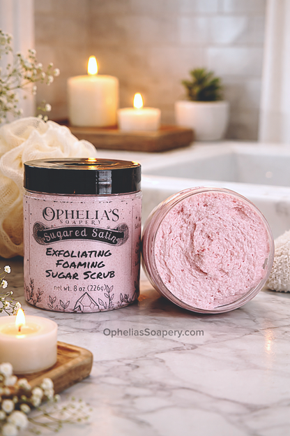 Ophelia's Soapery exfoliating foaming sugar scrub with packaging on a marble surface with candles and flowers.